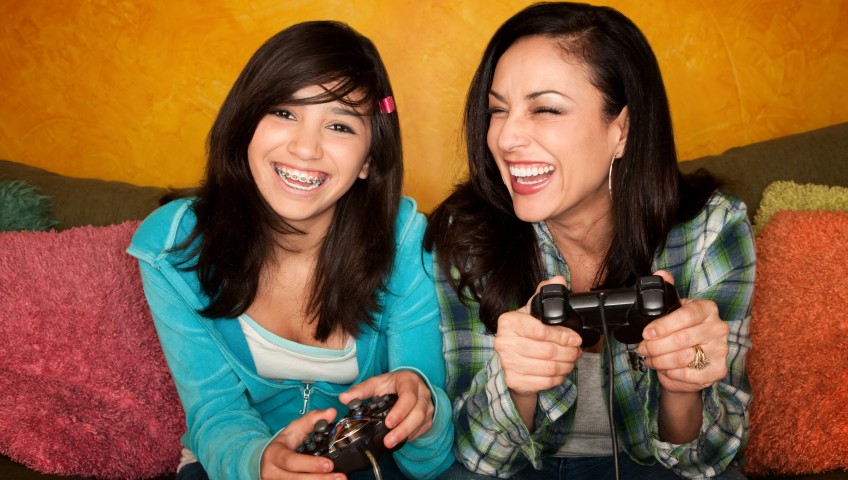 Smiling woman and teenage girl with braces and playing video games on couch