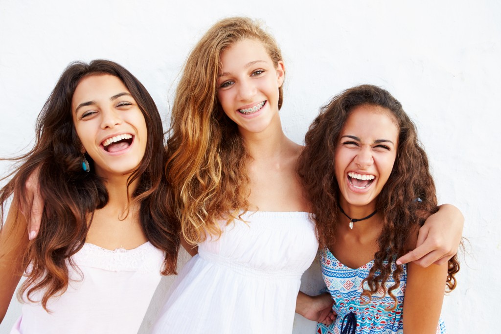 Three teenage girls laughing with arms over each other's shoulders 